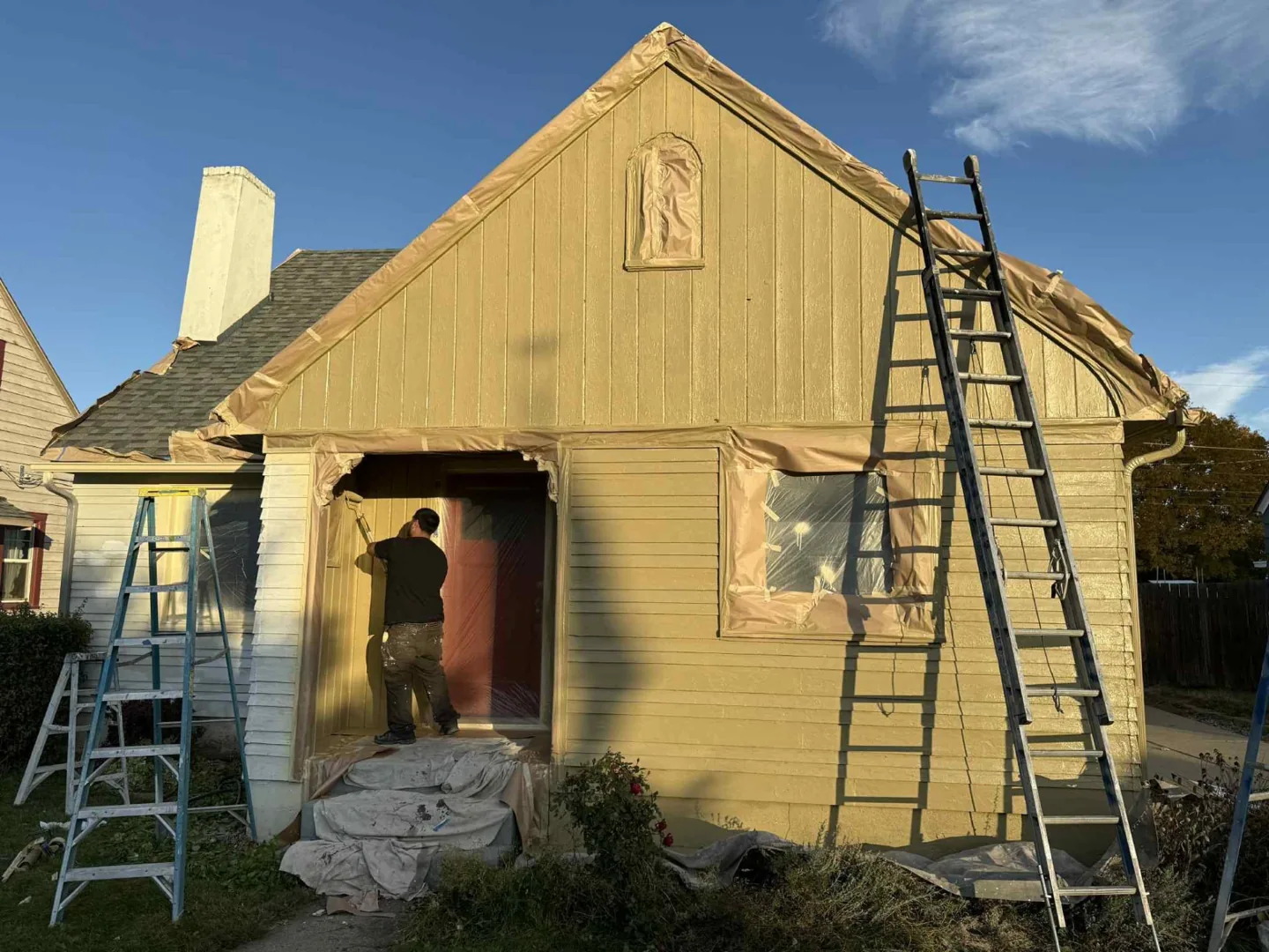 Tan house exterior repaint in progress with ladders beside the siding